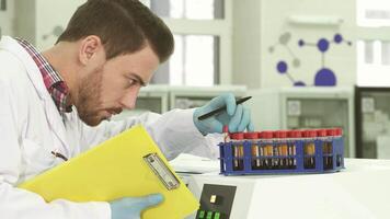 Focused laboratory assistant meticulously analyzes test tubes while documenting findings video