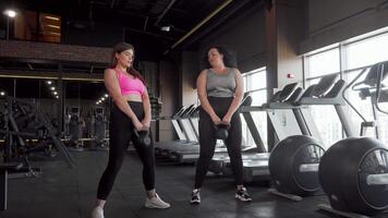 Two inspiring plus size female athletes squatting with kettlebells in a modern gym video