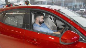 Confident young man smiling in a sleek new car at the dealership video