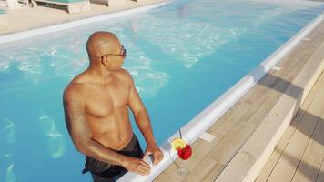 Handsome African man savoring a cocktail while relaxing by the shimmering pool video