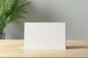 Blank greeting card on wooden table with greenery in soft natural light, minimalist scene photo