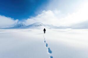A lone figure walks across a snowy expanse towards distant mountains under a clear blue sky. photo