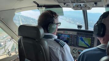 Pilots navigating small aircraft cockpit in flight, digital instruments and cityscape through windows video