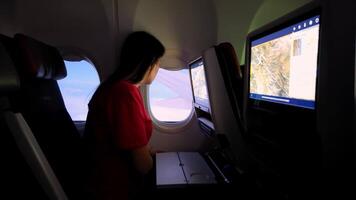 Woman looking through airplane window during flight, seat screen showing map and soft light inside cabin video