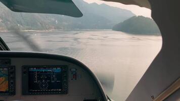 Cockpit view of small aircraft flying over calm mountain lake, digital instruments and scenic landscape ahead video