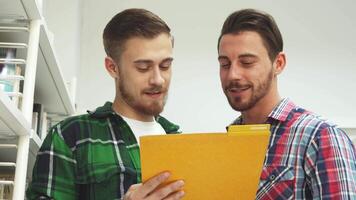 Two young men share a laugh while reading papers from a bright yellow folder video