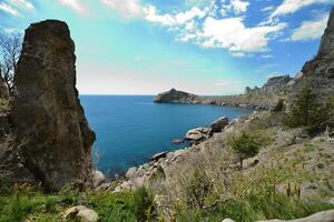 A cliff over a water body with a large rock in front photo