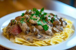 Classic beef stroganoff with mushrooms and creamy sauce, served with tender egg noodles and garnished with fresh parsley on a white plate photo