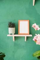 white frame mockup on shelf with decoration objects, rustic green wall photo