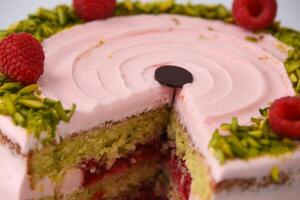 layered Raspberry Pistachio Cake frosted with light pink cream and garnished with fresh raspberries and chopped pistachios closeup side view of cafe dessert photo