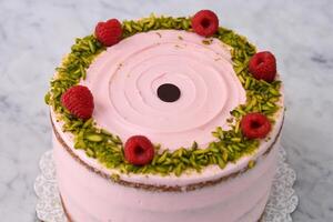 layered Raspberry Pistachio Cake round frosted with light pink cream and garnished with fresh raspberries and chopped pistachios closeup side view of delicious dessert photo