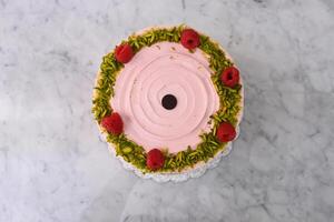 layered Raspberry Pistachio Cake round frosted with light pink cream and garnished with fresh raspberries and chopped pistachios top view of delicious dessert photo