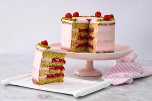 Elegant Raspberry Pistachio Layer Cake with Slice frosted with light pink cream and garnished with fresh raspberries and chopped pistachios side view of cafe dessert photo