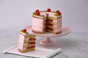 Elegant Raspberry Pistachio Layer Cake with Slice frosted with light pink cream and garnished with fresh raspberries and chopped pistachios closeup side view of cafe dessert photo