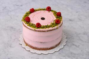layered Raspberry Pistachio Cake round frosted with light pink cream and garnished with raspberries and chopped pistachios side view of cafe delicious dessert photo