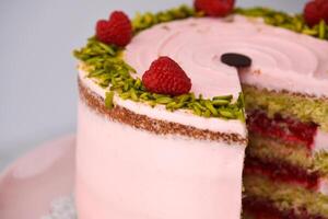 layered Raspberry Pistachio Cake frosted with light pink cream and garnished with fresh raspberries and chopped pistachios closeup side view of cafe delicious dessert photo