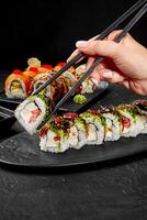 Woman using chopsticks picking sushi rolls from plate on black table photo