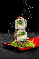 Stack of uramaki sushi rolls with sesame seeds falling on a red plate photo
