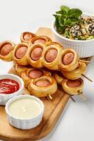 Sausage rolls skewers with dipping sauces and sesame salad on white background photo