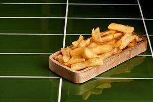 French fries served on wooden plate lying on green tiles photo