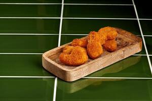 Breaded chicken nuggets served on wooden tray over green tiles photo