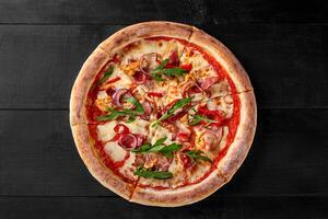 Delicious pizza with chicken, bacon, arugula and mozzarella on black wooden table photo