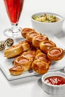 Sausage rolls on skewers served with ketchup and salad, refreshing drink on white table photo