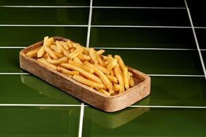 French fries served on wooden plate over green tiles surface photo