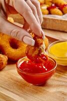 Woman dipping chicken nuggets into ketchup with onion rings and cheese sticks in background photo