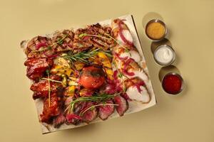 Grilled meat platter with chicken, pork, beef, vegetables and sauces, lying on pita bread photo