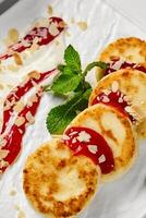 Syrniki with raspberry jam, almond flakes, sour cream and mint on white plate photo