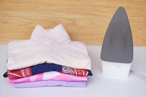 Electric iron and stack of folded clothes on table. Concept, daily chore, household. ironing and folded clothes for neat and clean. photo