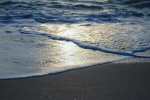 Closeup wave sufing on the sand beach with reflection of the sun light on the surface of the water photo