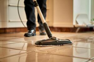 Close up of a person mopping a tiled floor with a flat mop in a brightly lit room indoors photo