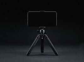 A sleek black smartphone mounted on a compact tripod against a dark minimalist background setup shot photo