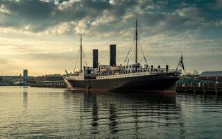 A large black and white ship docked in a harbor with buildings and cloudy skies in the background photo
