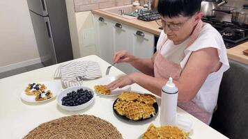 Senior woman adding whipped cream to waffles in kitchen video