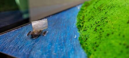 A small boat on a table with a green field photo