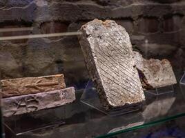 An old stone slab is on display in a glass case photo