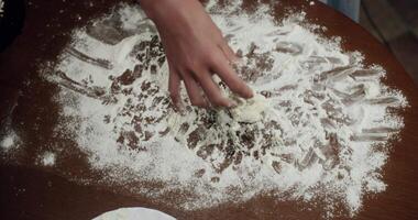 Professional baker carefully kneading fresh dough on rustic wooden surface, methodically shaping small dough portions and arranging finished balls on pristine white plate video