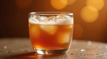A close-up of a glass containing amber beverage with ice, set against a blurred bokeh background. photo