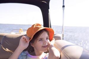 Close-up of a little girl in a panama hat smiling on a yacht. A cute child is having fun and relaxing on board the ship. photo