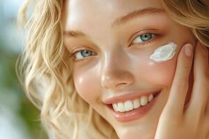 Caucasian woman applying moisturizing cream with visible dab on cheek. Skincare routine for hydration and smooth skin care photo