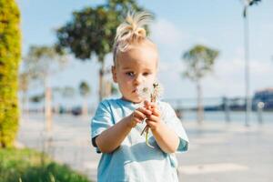 Little child blowing dandelion seeds on a sunny day at the waterfront photo