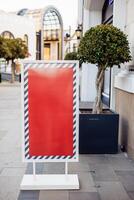 Blank advertising board stands on sidewalk near trees and modern architecture in daytime photo