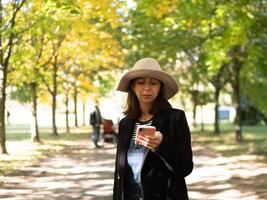 A woman happily enjoys a beautiful day outdoors, focused on her phone amidst the vibrant autumn foliage photo