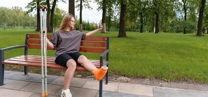 Teenage girl with a cast on her leg seated on a park bench, taking a thoughtful selfie to document the difficulties of her injury and the time she's had to spend in recovery during the summer photo