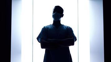 Silhouette of a surgeon in scrubs with arms crossed in a bright setting photo