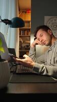 Tired freelancer procrastinating at home office, scrolling phone instead of working. Unproductive man using smartphone at home desk video