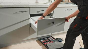 Man assembling kitchen drawer in cabinet. Handyman installing and adjusting drawer slide mechanism in contemporary kitchen. Furniture installation video